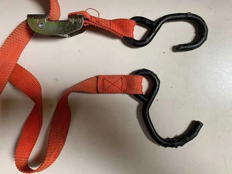 Worn-out orange tie-down strap with bent and degraded S-hooks showing clear signs of aging and damage