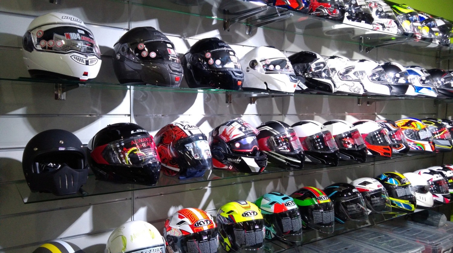 Assorted motorcycle helmets displayed on glass shelves, including budget and branded models