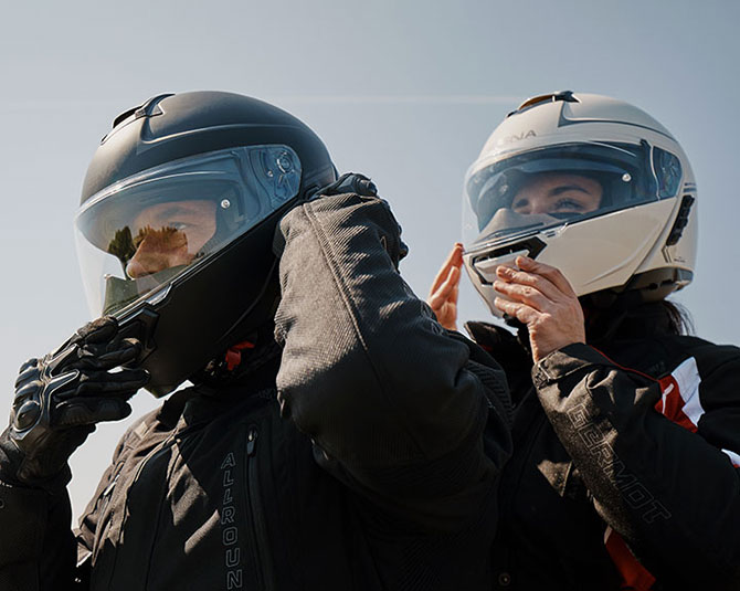 Two motorcyclists wearing full-face helmets preparing for a ride, one in black and one in white.