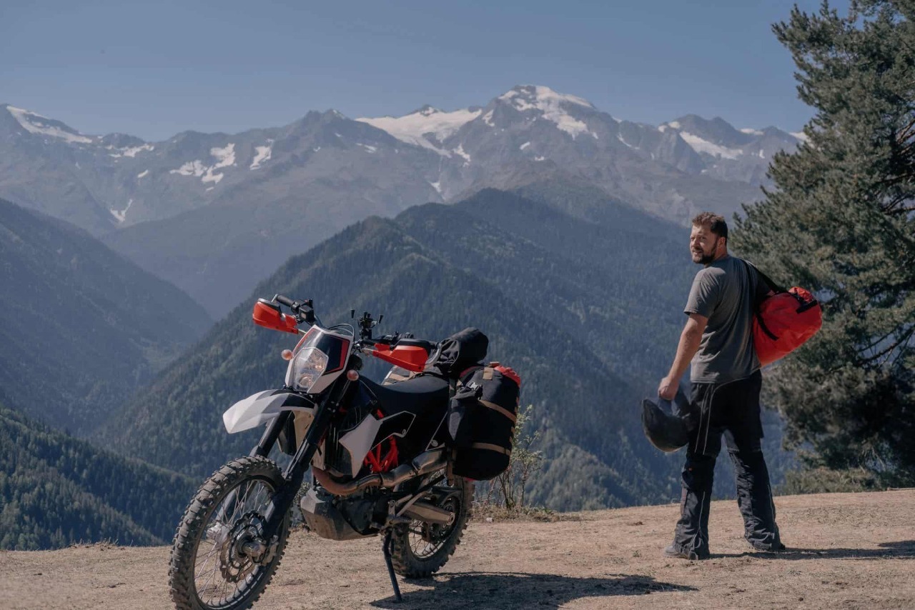 Adventure rider with gear and dual-sport motorcycle overlooking mountain valley
