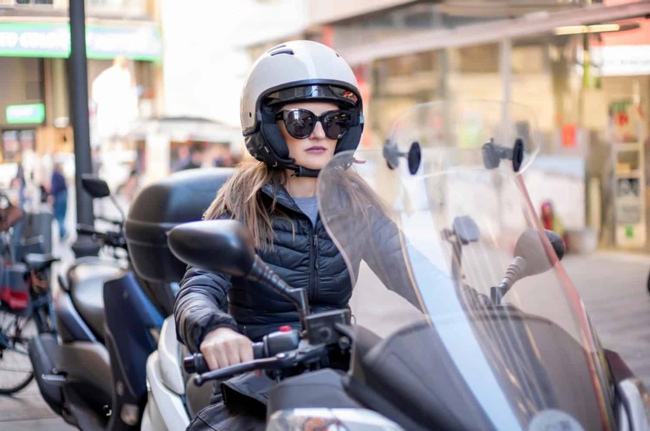 Woman in open-face helmet riding a scooter in the city