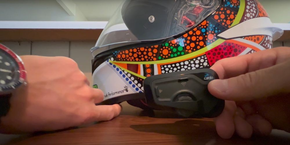 Motorcyclist pointing to the mounted microphone inside a helmet while holding a Cardo Freecom 4X unit.