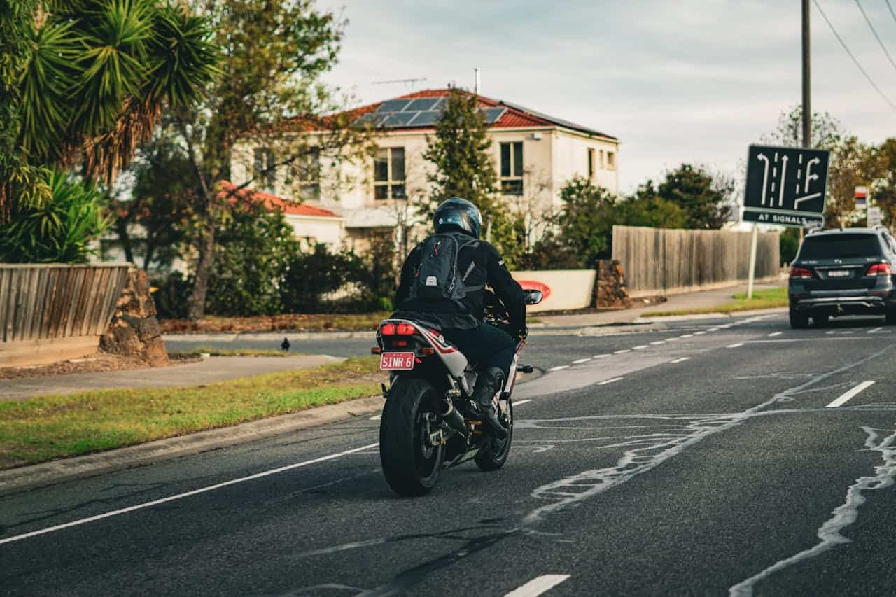 Motorcyclist riding through suburban Australian streets wearing a helmet and backpack.