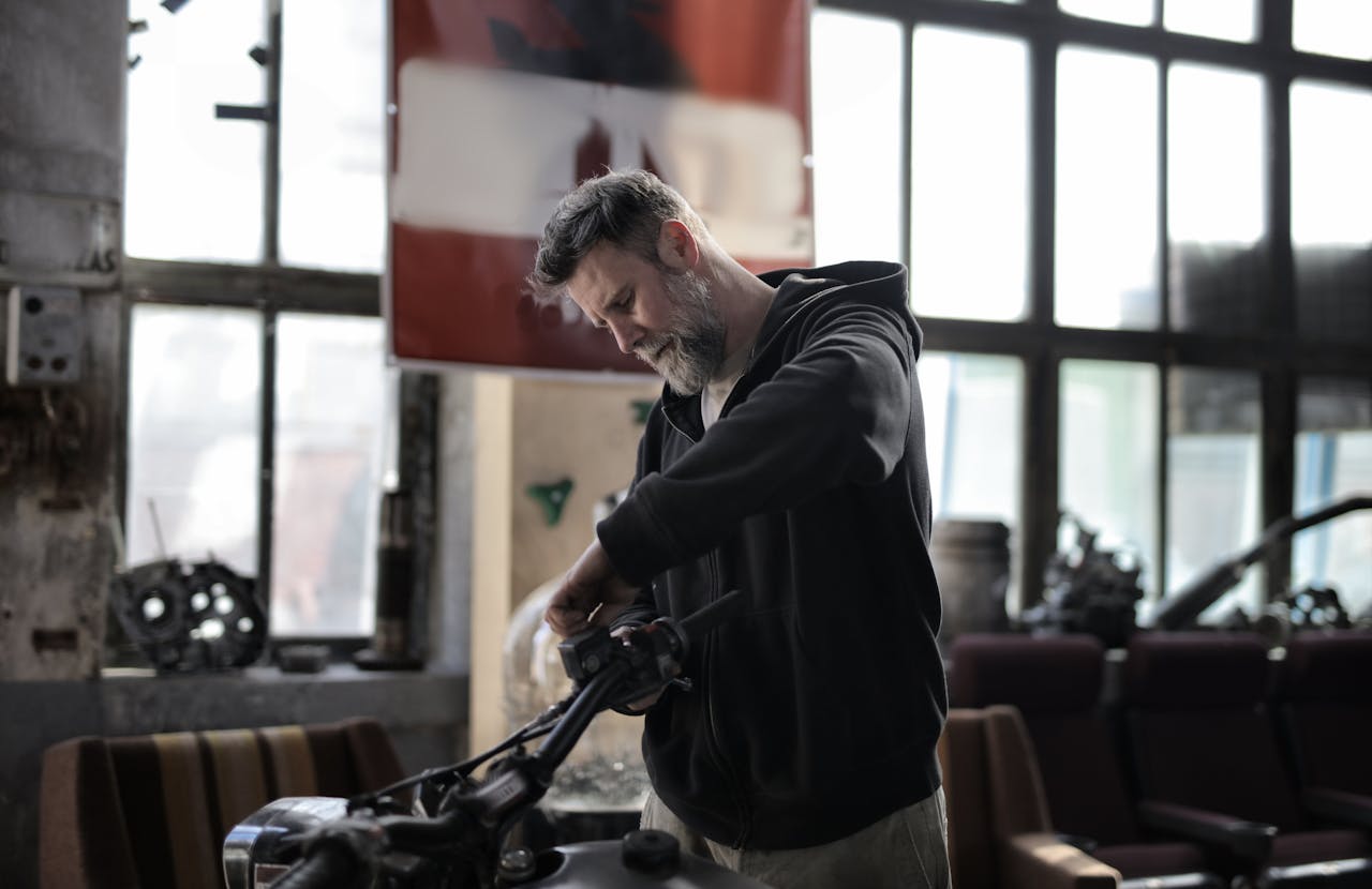 Man working on motorcycle controls inside a workshop using hand tools