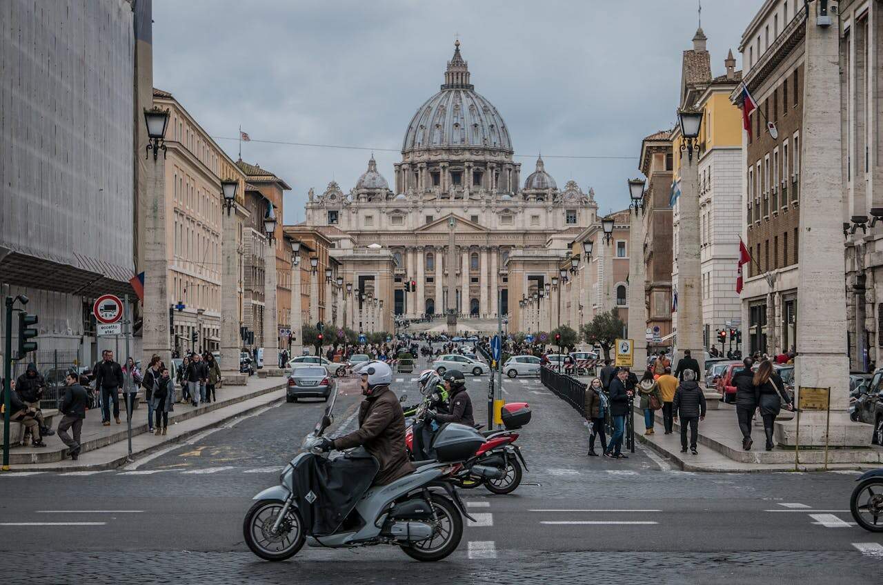 Scooter riders in Rome with St. Peter’s Basilica in the background, highlighting typical urban motorcycling in Europe
