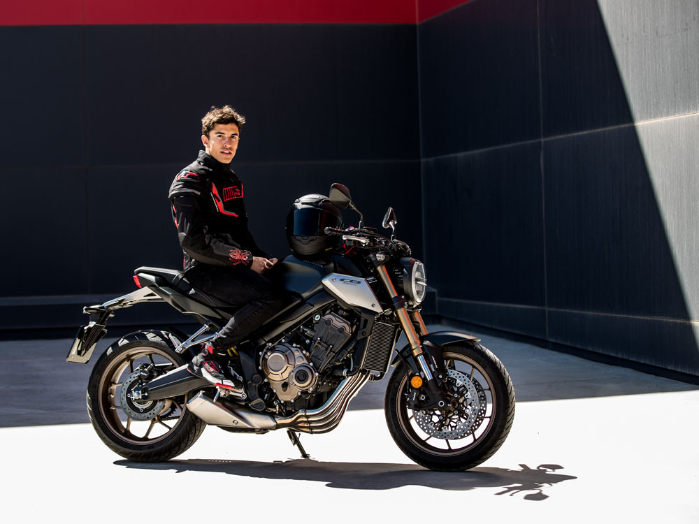 Rider seated on sport bike with Shoei NXR2 helmet resting on tank, urban background