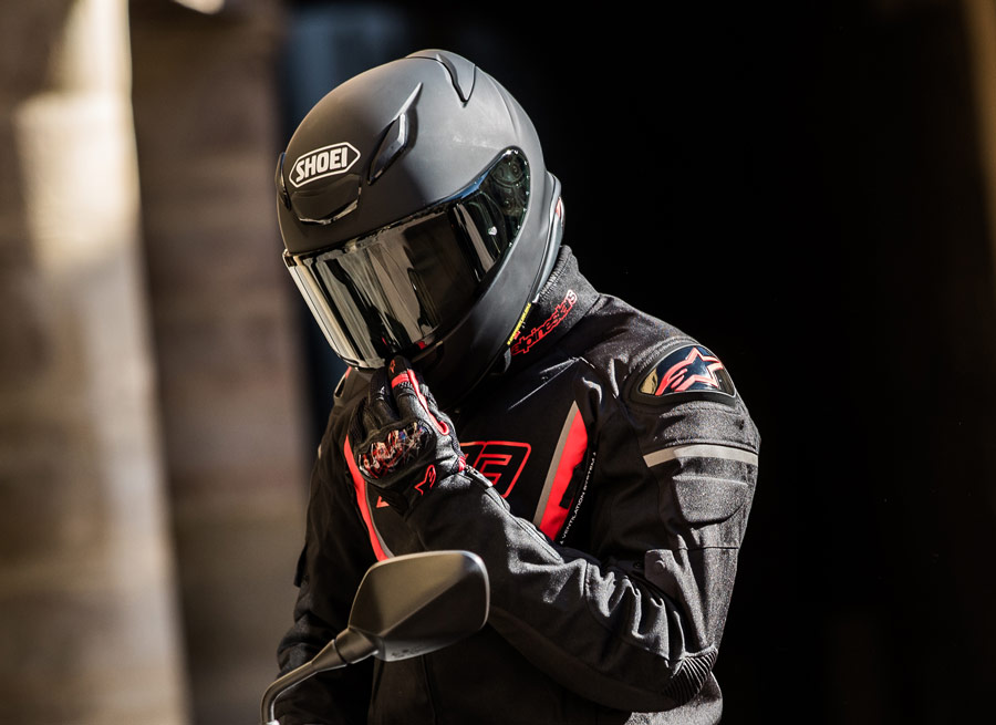Rider wearing a matte black Shoei helmet with a closed visor, adjusting chin strap