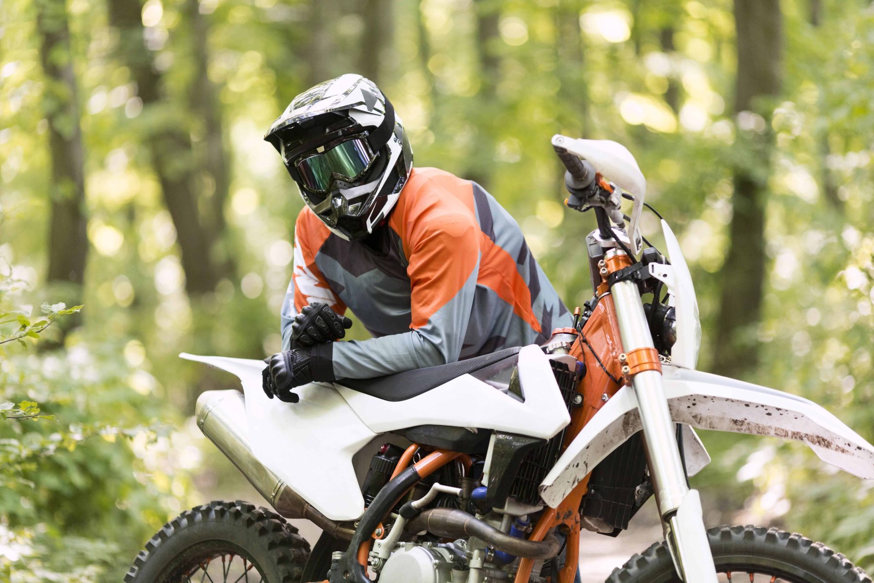 Off-road rider wearing a full-face ADV helmet and gear, sitting on a dirt bike in the forest