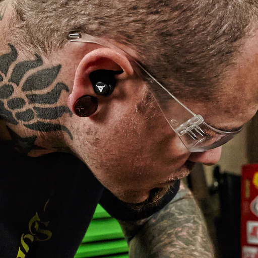 Close-up of a man wearing custom-moulded Decibullz earplugs and safety glasses, showing snug fit and ear seal