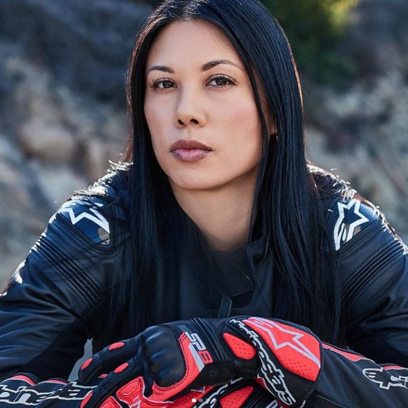 Woman in full motorcycle gear wearing red Alpinestars gloves with carbon knuckle protection.
