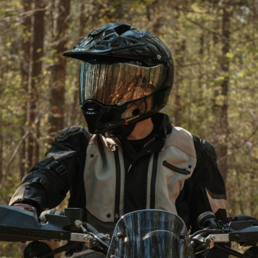 Rider wearing a Shoei Hornet X2 ADV helmet with reflective visor in the forest, front view on a dual-sport motorcycle.