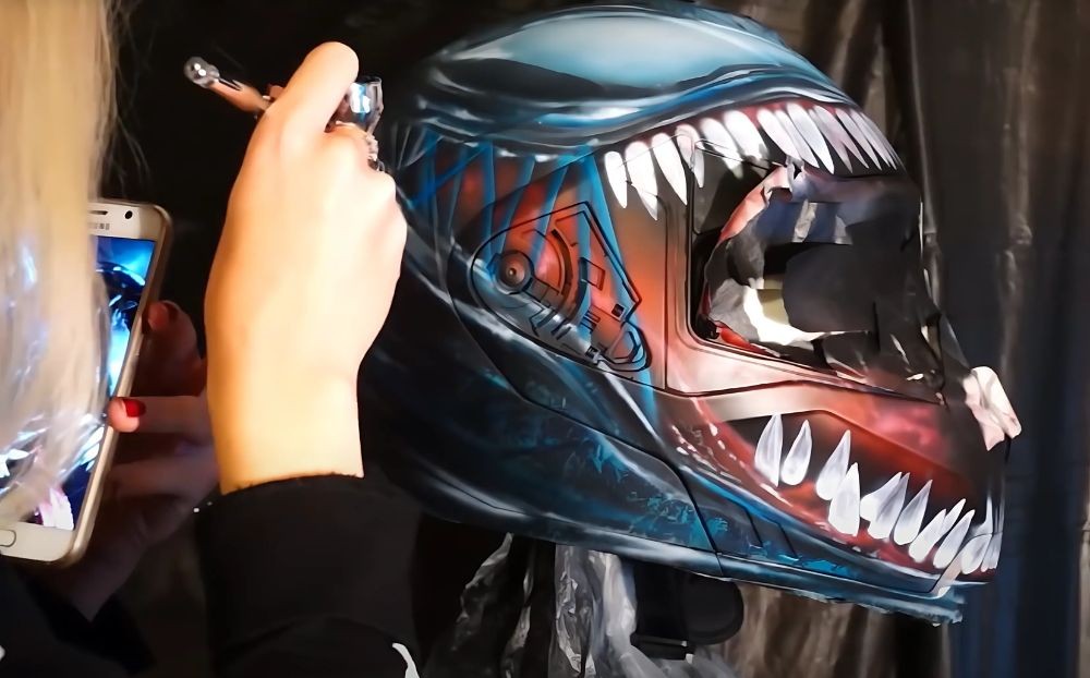 Artist airbrushing a custom Venom-themed design onto a modular motorcycle helmet.