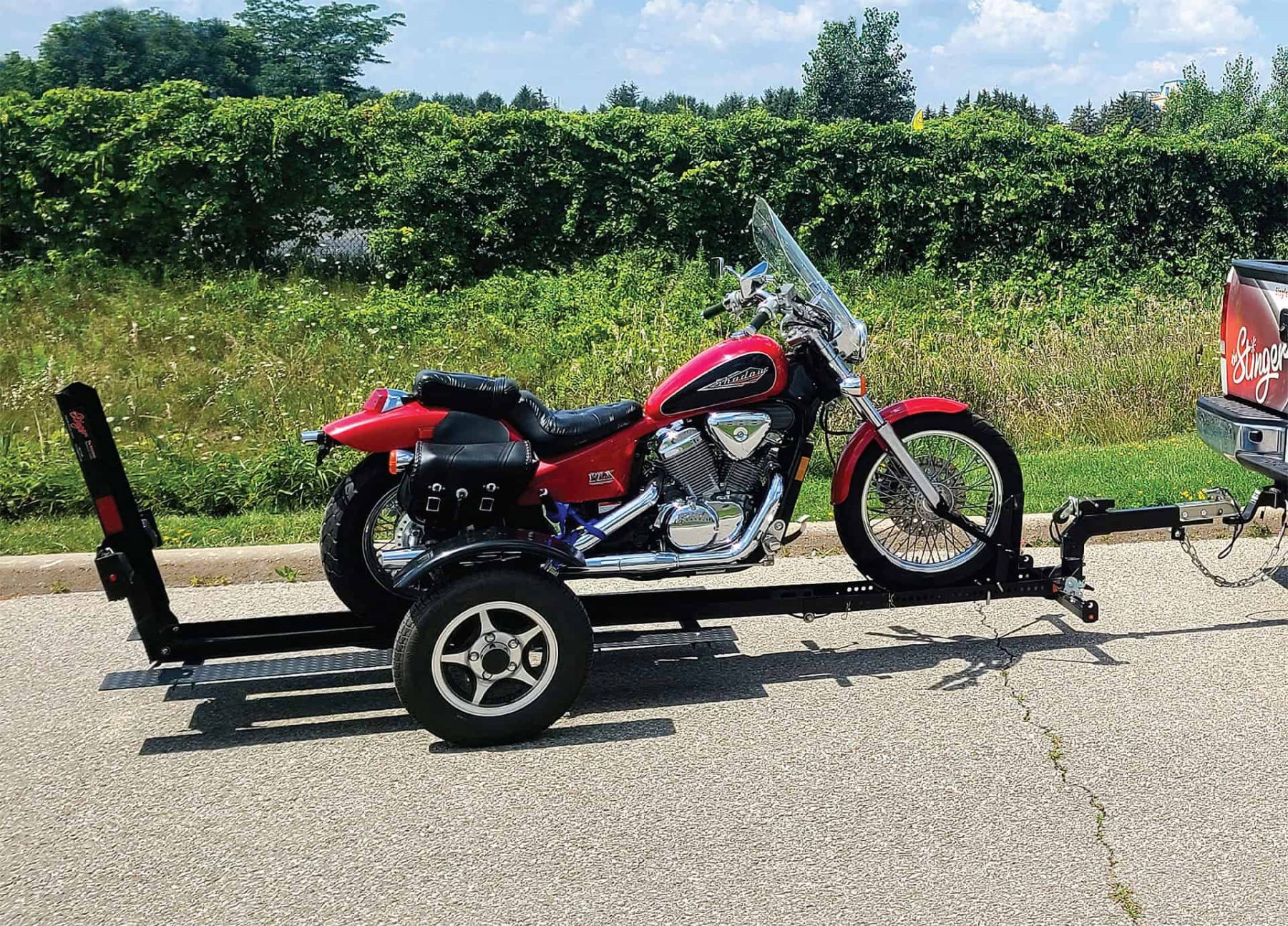 Red cruiser motorcycle secured on a rail-style motorcycle trailer hitched to a pickup.