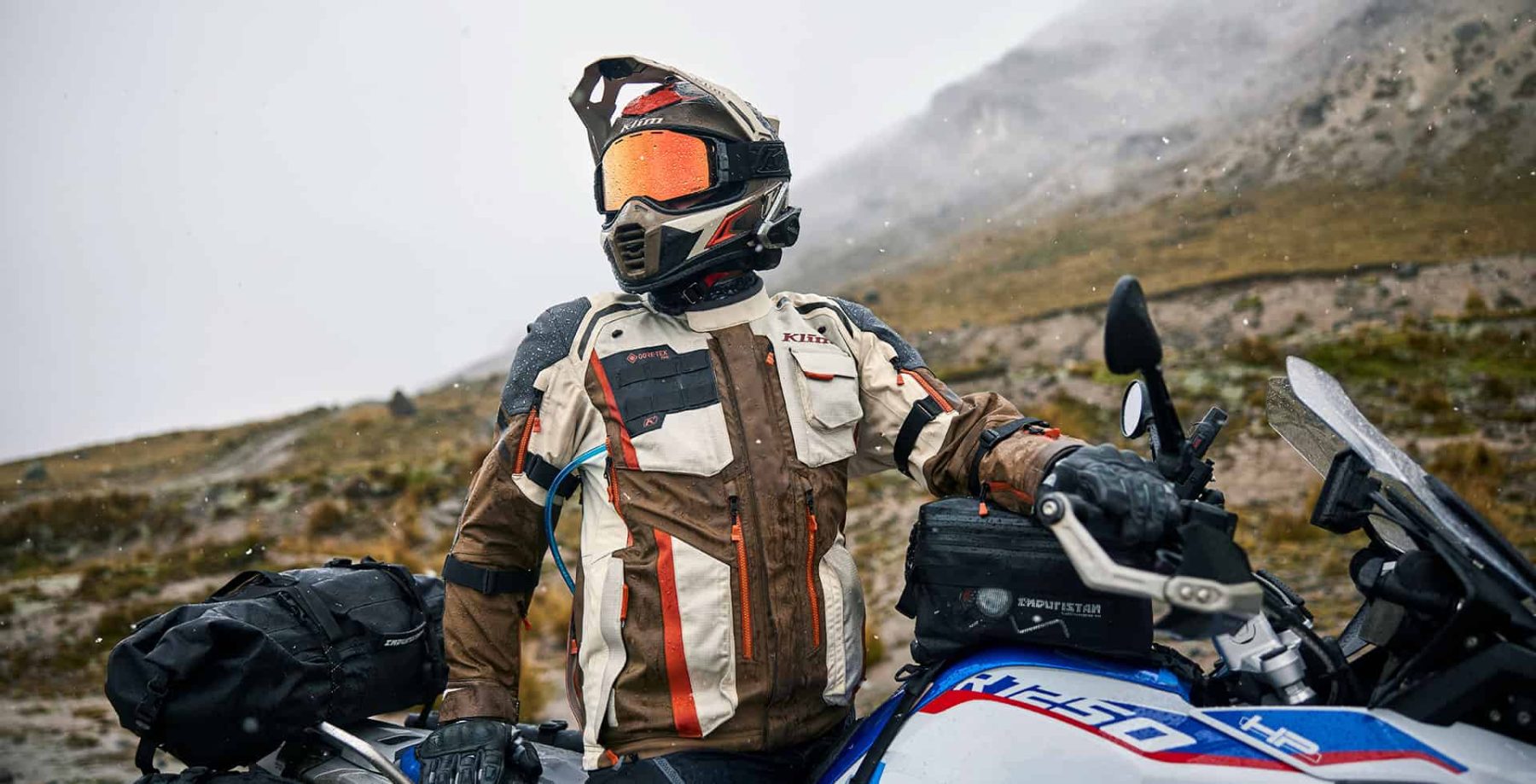 Adventure rider wearing a Shoei helmet with Sena 50S headset and Klim jacket, stopped on a BMW GS motorcycle in the rain.