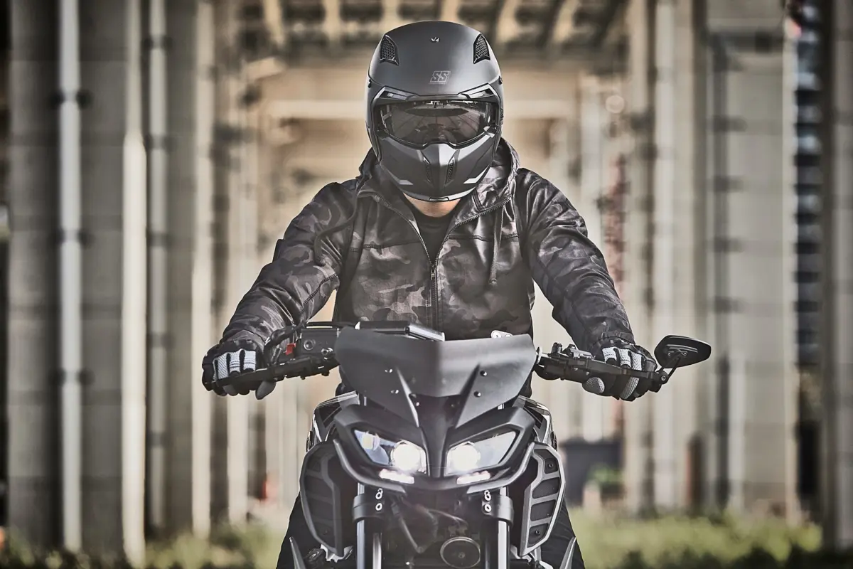 Motorcyclist wearing Speed & Strength SS2400 helmet and tactical jacket, riding under an industrial overpass.