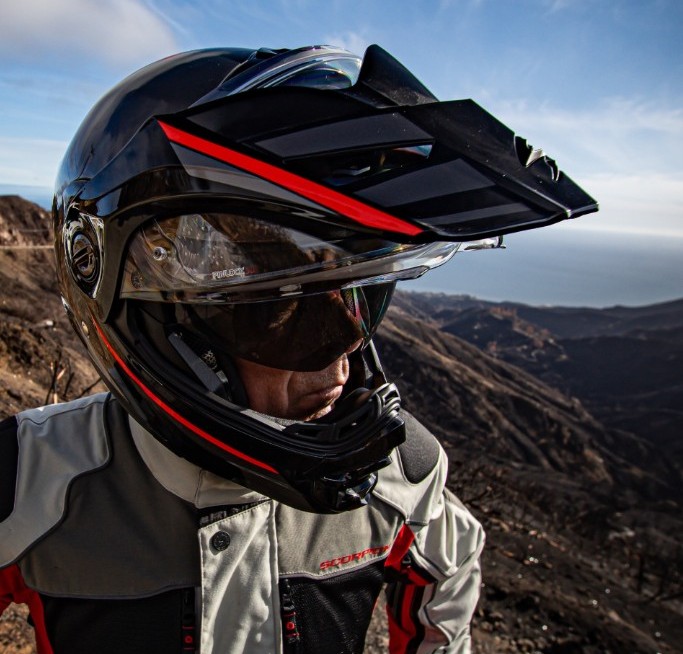 Adventure rider wearing ScorpionEXO AT960 helmet with peak and sun visor overlooking mountain trails