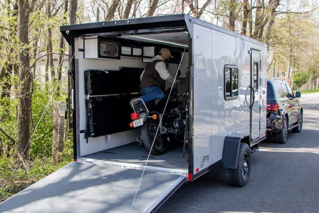 Rider loading a motorcycle into an enclosed trailer hitched to an SUV.