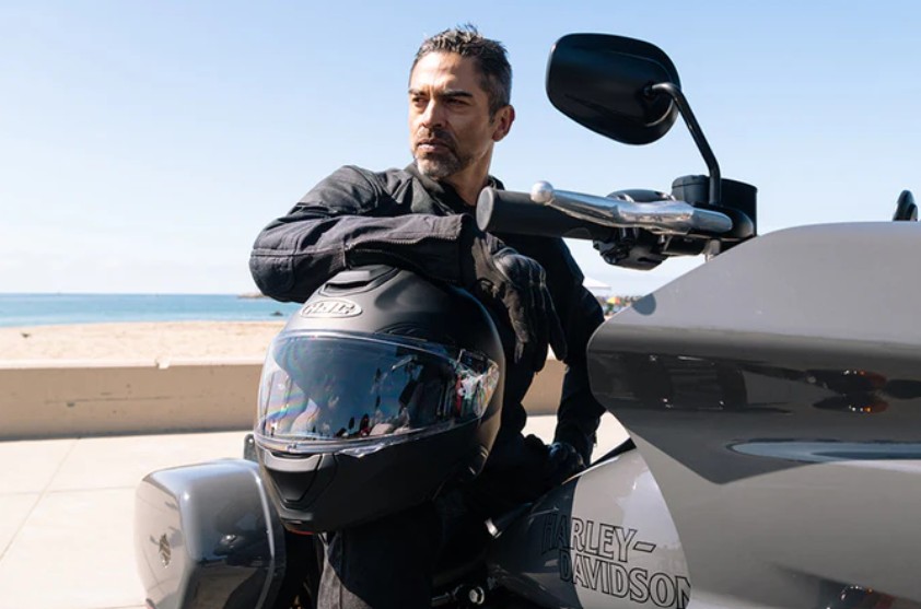 Rider leaning on a Harley-Davidson while holding an HJC RPHA 91 modular helmet
