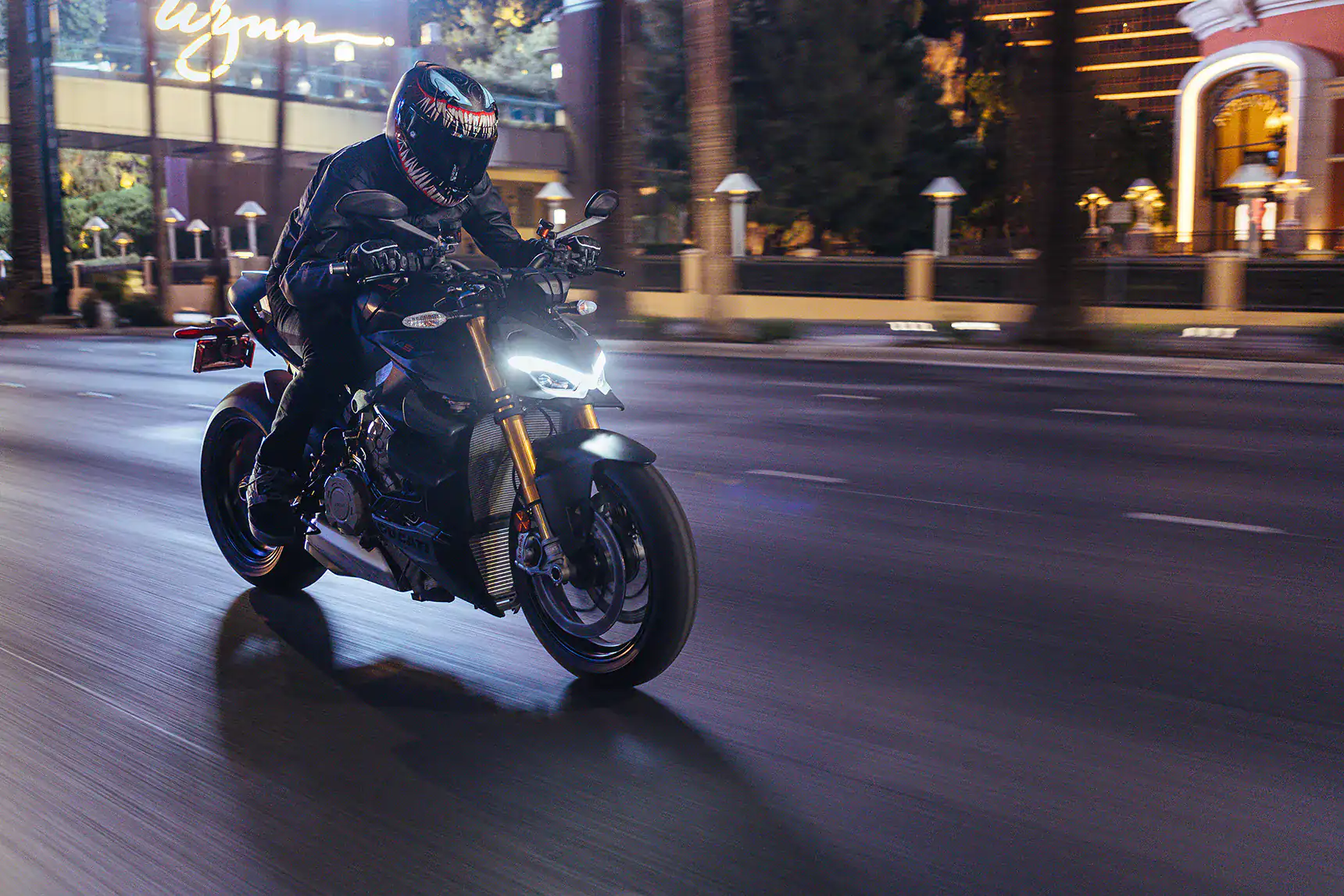 Rider wearing a Venom-themed helmet on a sportbike at night in the city.