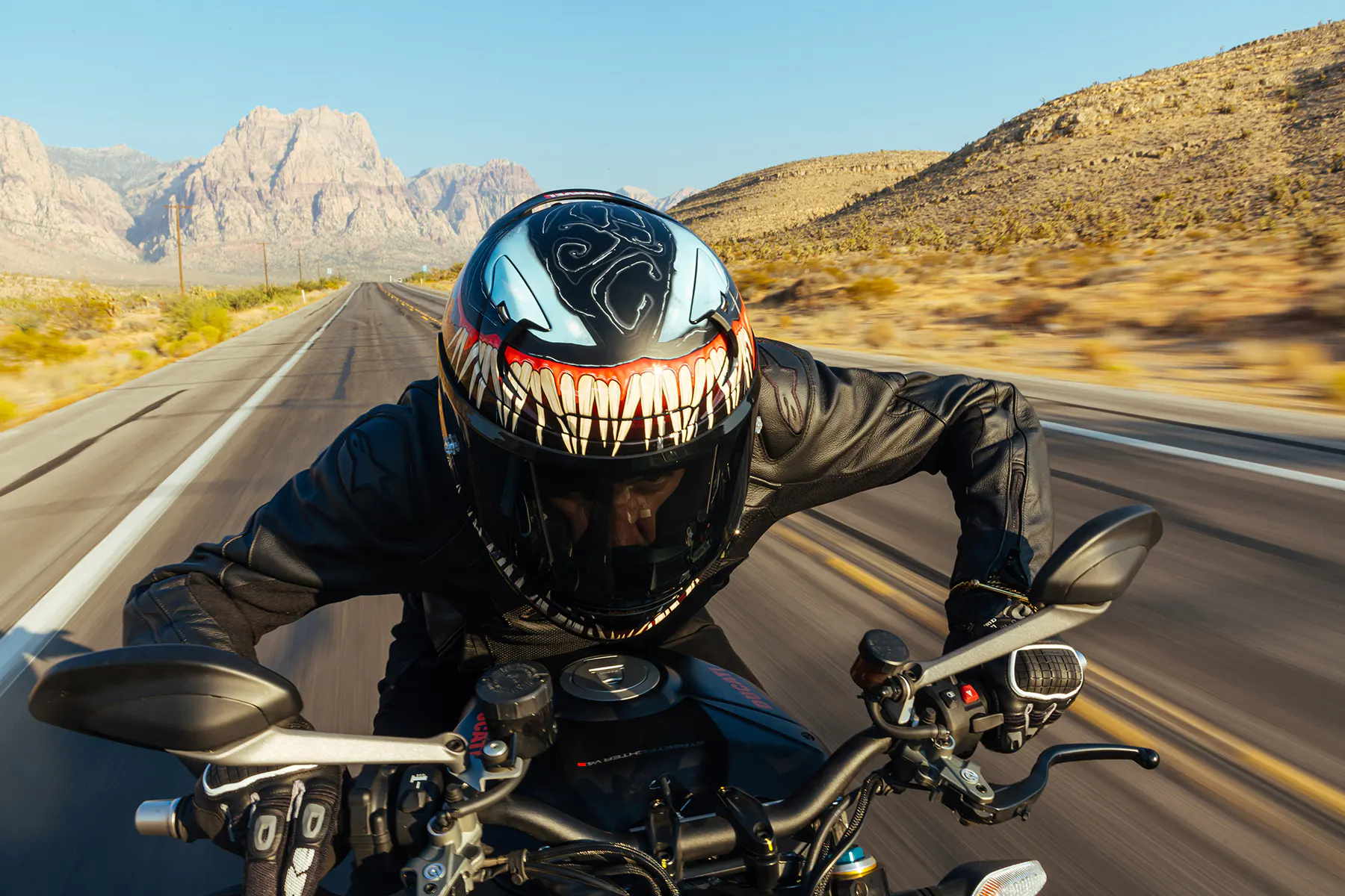 Rider in full tuck wearing HJC RPHA 12 Venom helmet on an open desert highway.