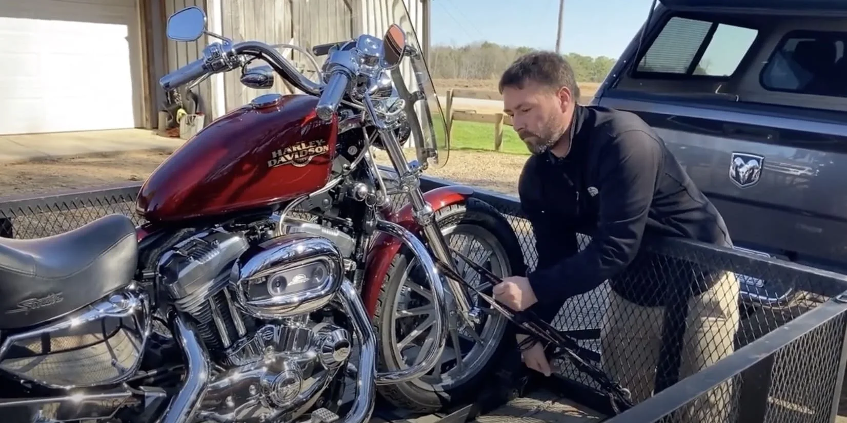 Man securing a Harley-Davidson motorcycle on a trailer using a ratchet strap.