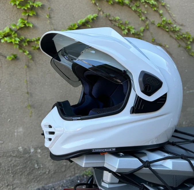 White Arai XD-5 adventure motorcycle helmet with peak visor and face shield, side view on a bike rack outdoors.