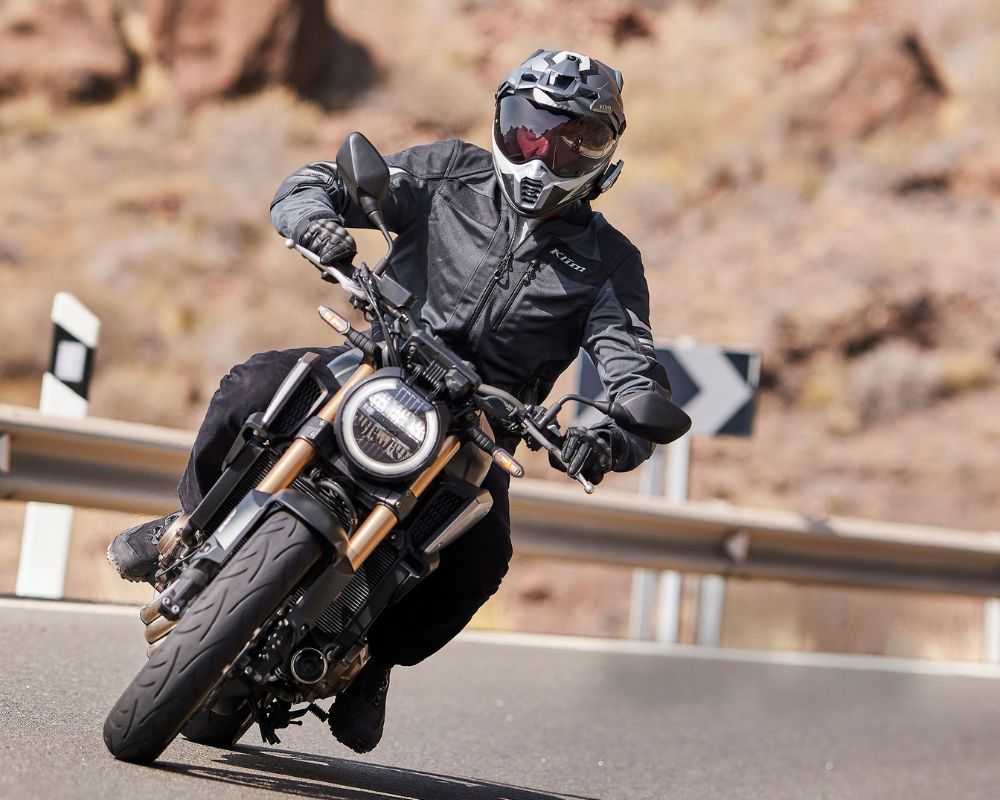 Rider wearing Klim Induction Pro jacket leaning into a curve on a naked motorcycle