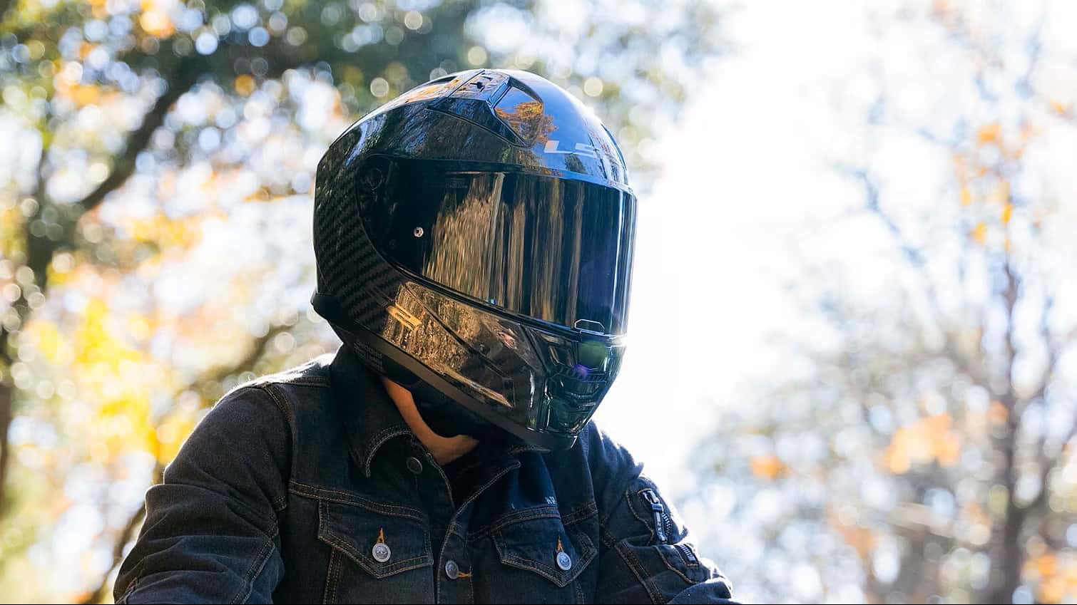 Rider wearing an LS2 Citation II Carbon helmet with mirrored visor, framed by autumn trees in the background.