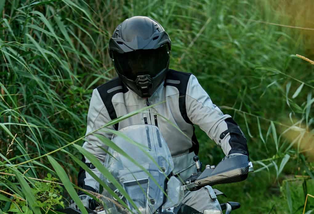 Rider wearing a Sedici Adventure Modular helmet and textile jacket while exploring a grassy off-road trail on an ADV motorcycle.