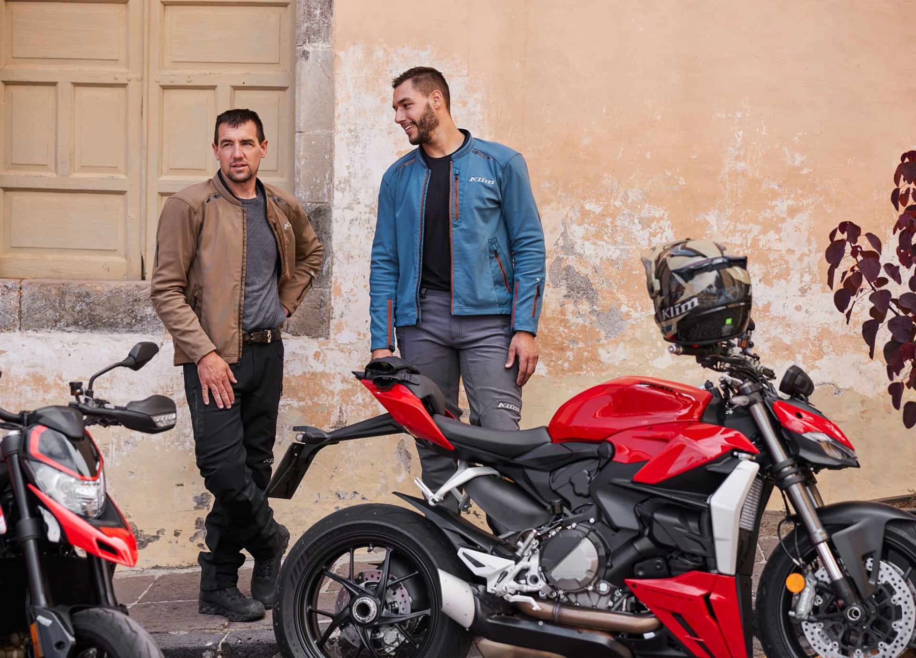 Two riders off the bike, one wearing Klim Marrakesh jacket styled like casual outerwear.