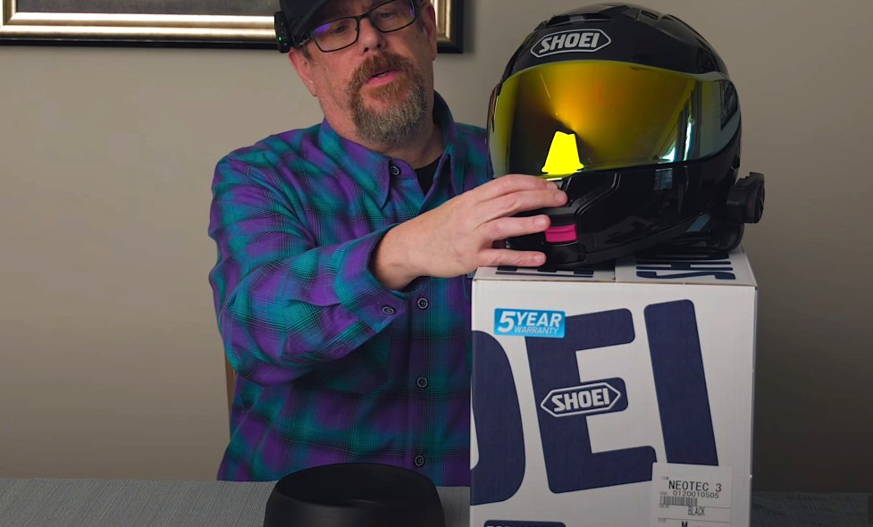 Reviewer holding Shoei Neotec 3 modular helmet with tinted visor, demonstrating central visor lock