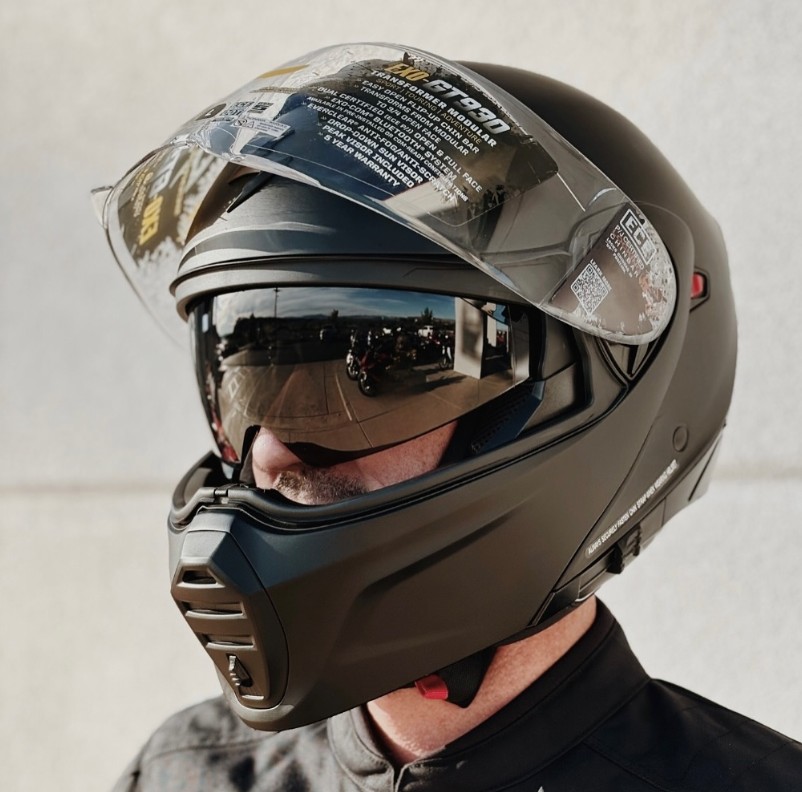 Rider wearing a matte black Scorpion EXO-GT930 helmet with Everclear visor raised and SpeedView sun visor in use.