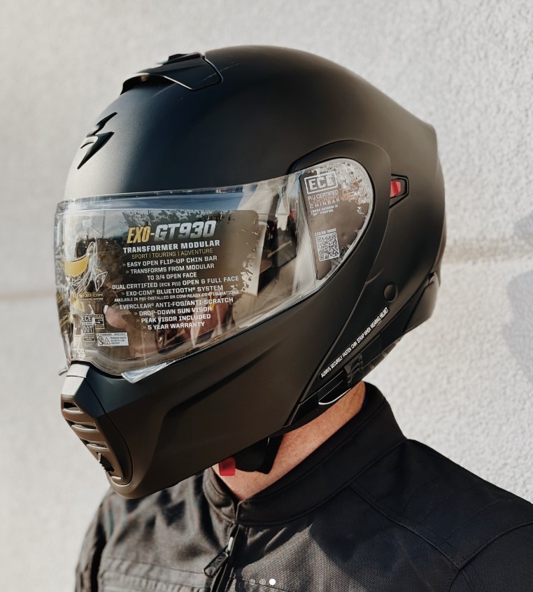 Rider wearing a matte black Scorpion EXO-GT930 modular helmet with visor sticker, side view.