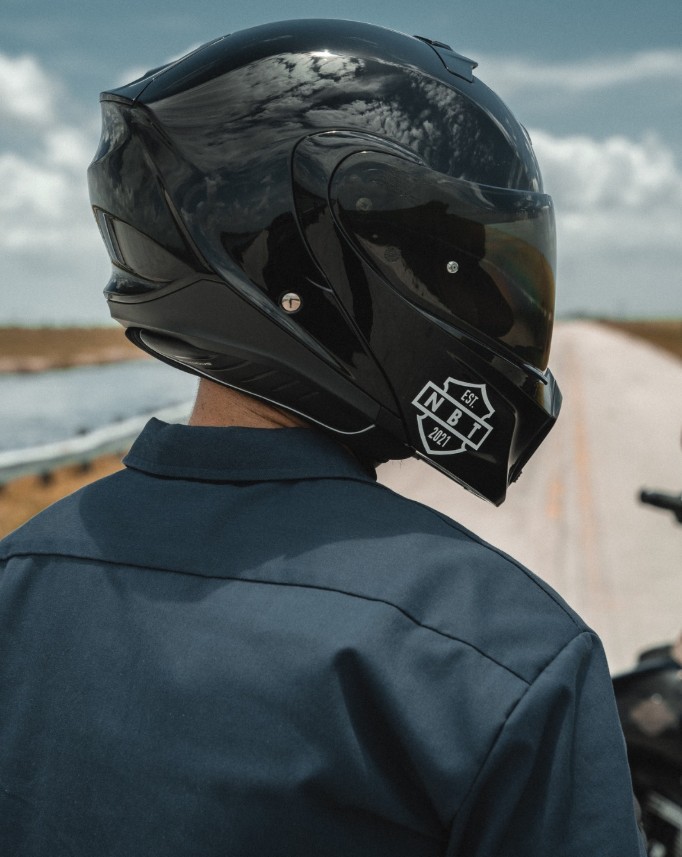 Rider wearing a glossy black Scorpion EXO-GT930 modular helmet, rear and side view under a bright sky.