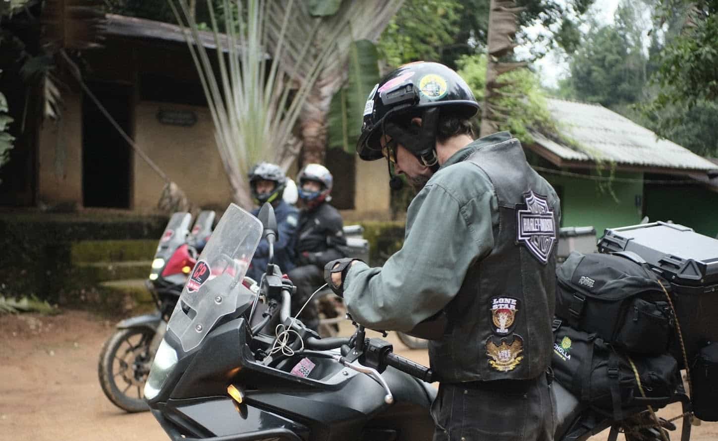 Motorcyclist preparing gear on a touring bike, wearing a helmet with a Cardo Packtalk Edge communicator.