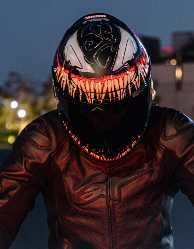 Motorcyclist wearing an HJC RPHA 12 Venom helmet with official Marvel graphics and a dark leather jacket at dusk.