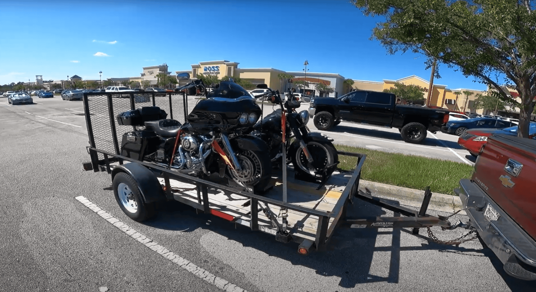 Two Harley-Davidson motorcycles secured with ratchet straps on a flatbed trailer hitched to a pickup truck.