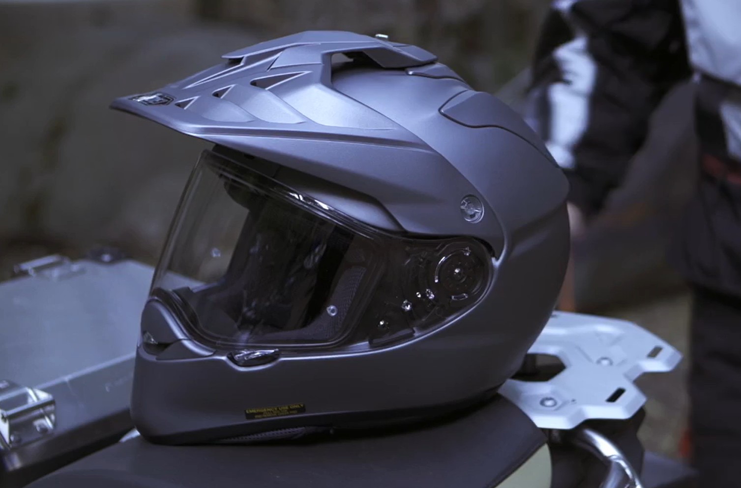 Matte gray Shoei Hornet X2 adventure motorcycle helmet with peak visor, side view resting on a bike.