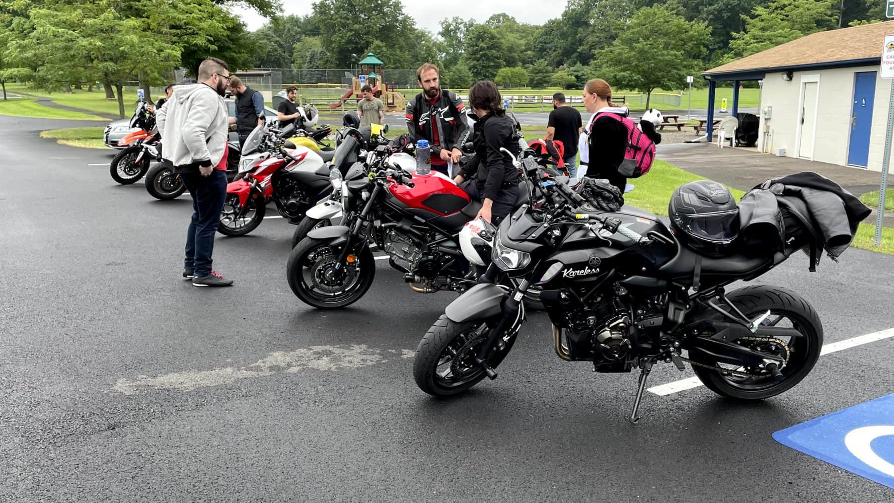 Group of riders gathered in a parking lot with motorcycles lined up; a Shoei RF-1400 full-face helmet rests on a black bike seat.