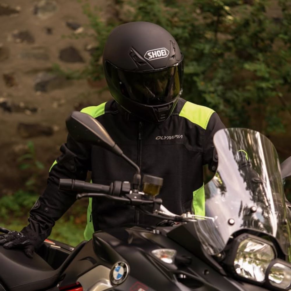 Rider wearing a matte black Shoei RF-SR helmet and Olympia hi-vis jacket, seated on a BMW adventure motorcycle.