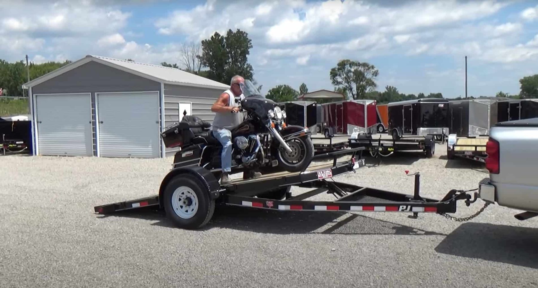 Rider loading a Harley-Davidson onto a tilt deck motorcycle trailer hitched to a truck.