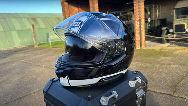 Shoei GT-Air 3 motorcycle helmet in gloss black with visor raised, placed on a pannier case outdoors.