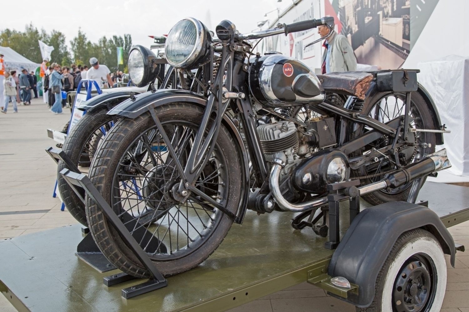 Vintage motorcycles secured on an open flatbed trailer at an outdoor event.