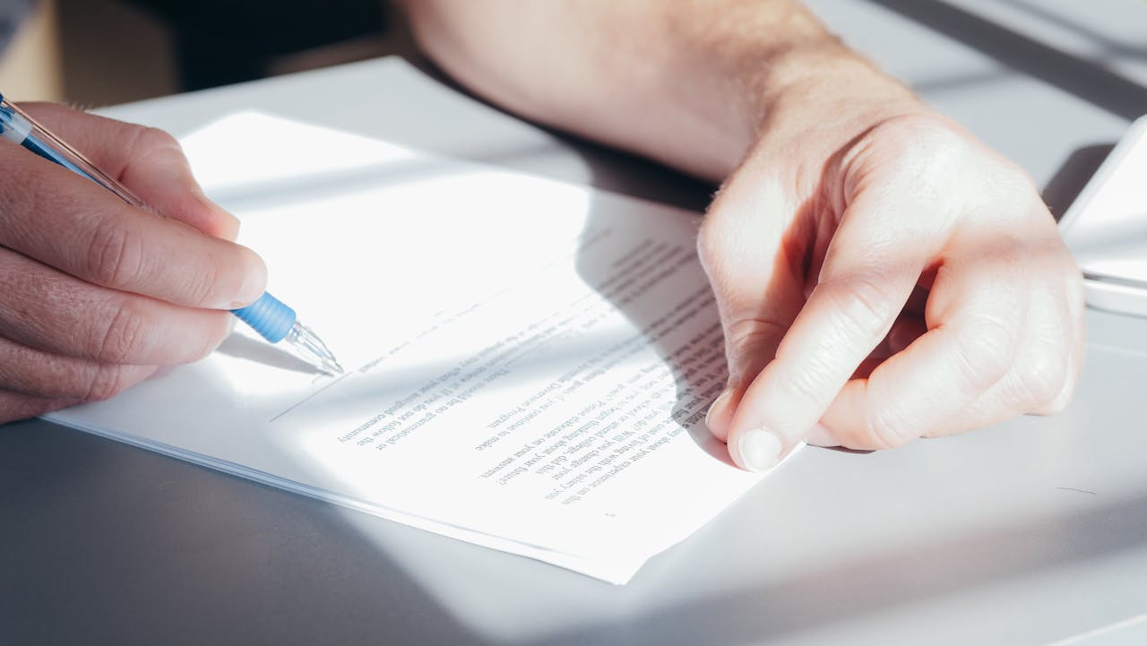 Close-up of a person holding a pen and reviewing a document before signing.