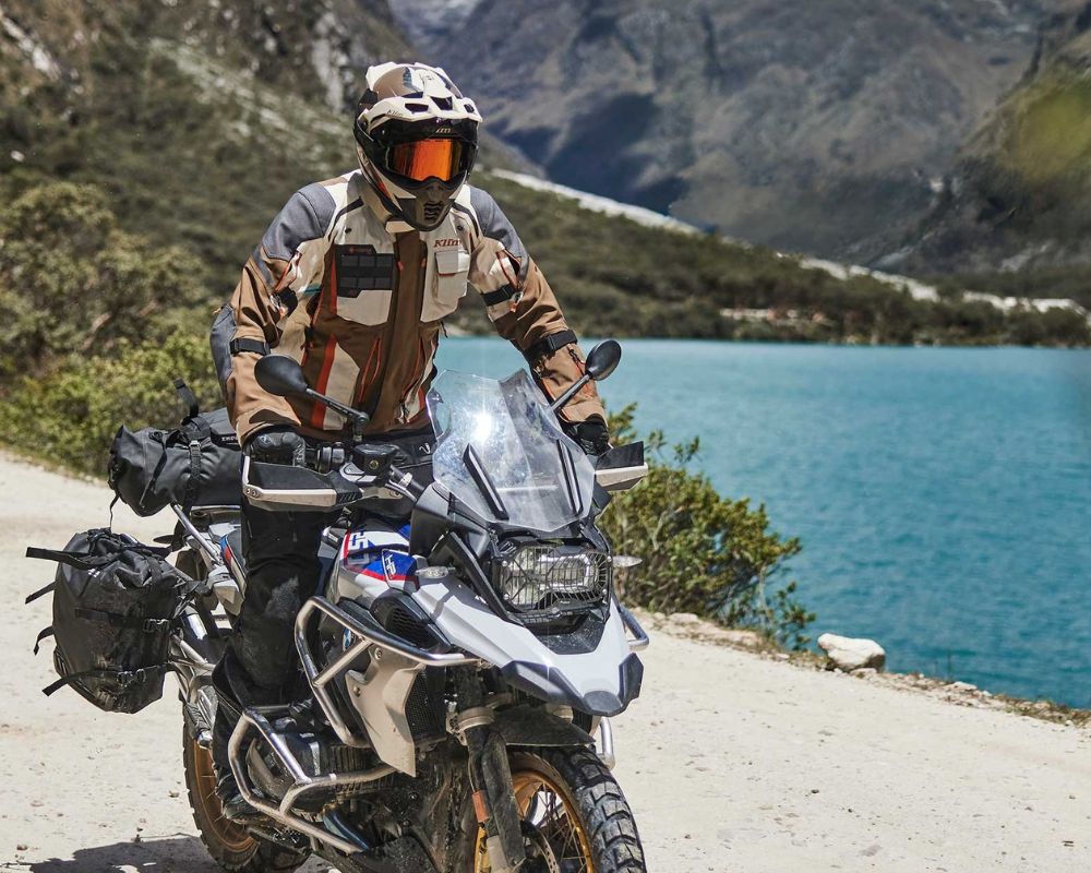 Rider wearing Klim Krios Pro helmet on ADV bike near mountain lake