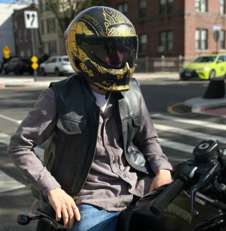 Motorcyclist wearing a black leather vest and gold-detailed helmet, showcasing classic biker style and street attitude.