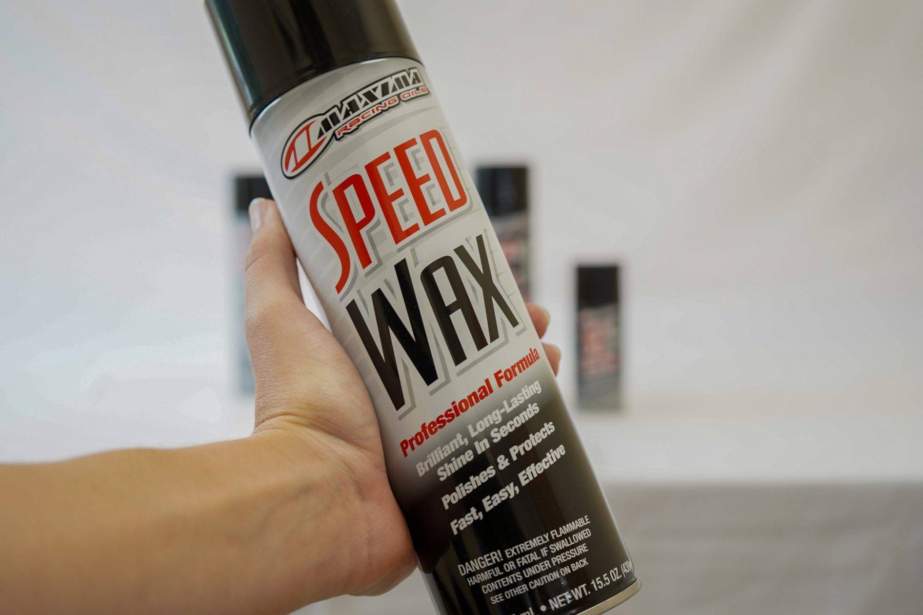 Hand holding a can of Maxima Speed Wax motorcycle detail spray, designed to clean, shine, and protect bike surfaces.