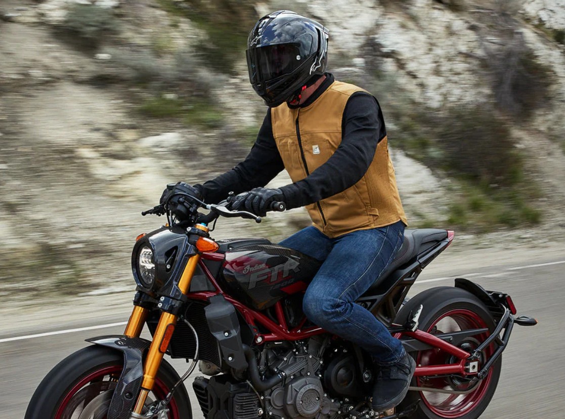 Motorcyclist wearing a tan airbag vest rides a naked bike on a winding road, showcasing modern safety gear in action.