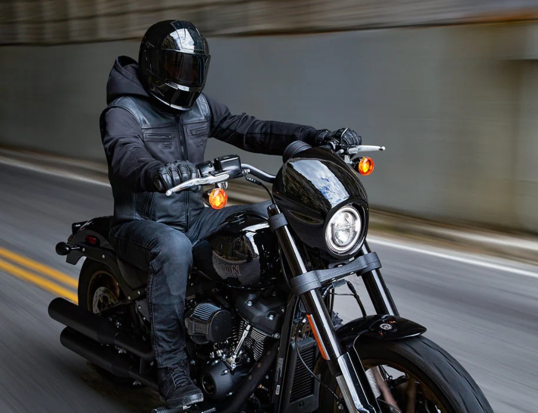 Motorcyclist wearing a black algorithm-based airbag vest and full-face helmet rides through a tunnel on a Harley-style cruiser.