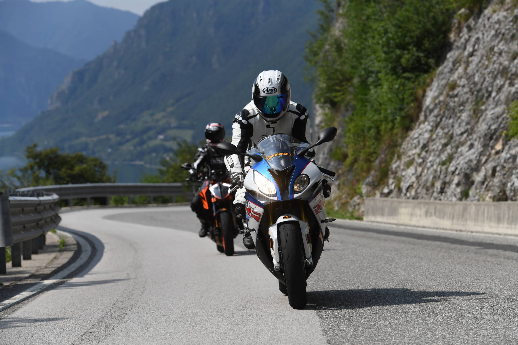 Two sportbikes cornering on a mountain road, front rider using Continental Race Attack 2 tires for grip and stability